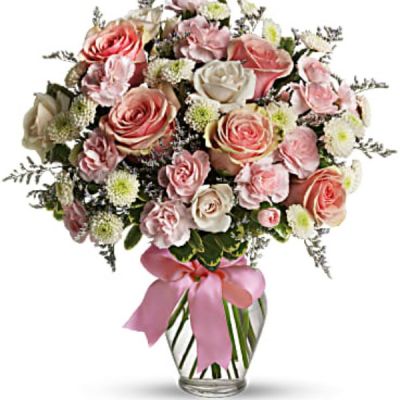Pretty pink roses, spray roses and miniature carnations, white button spray chrysanthemums, lavender limonium and green pittosporum fill a spring glass vase that's wrapped with a pink satin ribbon. It's confection perfection!